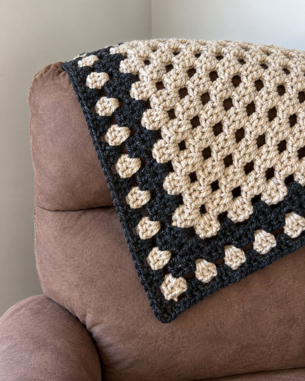 Corner detail of oatmeal and charcoal crochet reading blanket on brown recliner