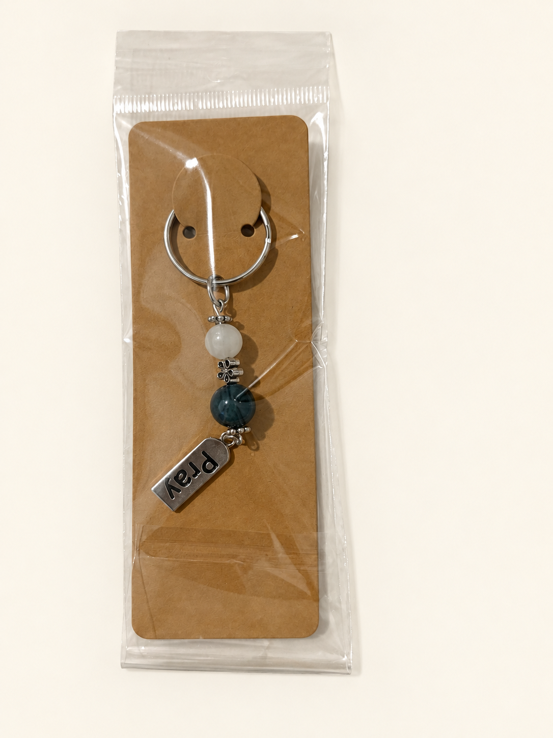 Pray Word Bead Keychain with white and deep teal beads, packaged on a kraft card in a clear sleeve